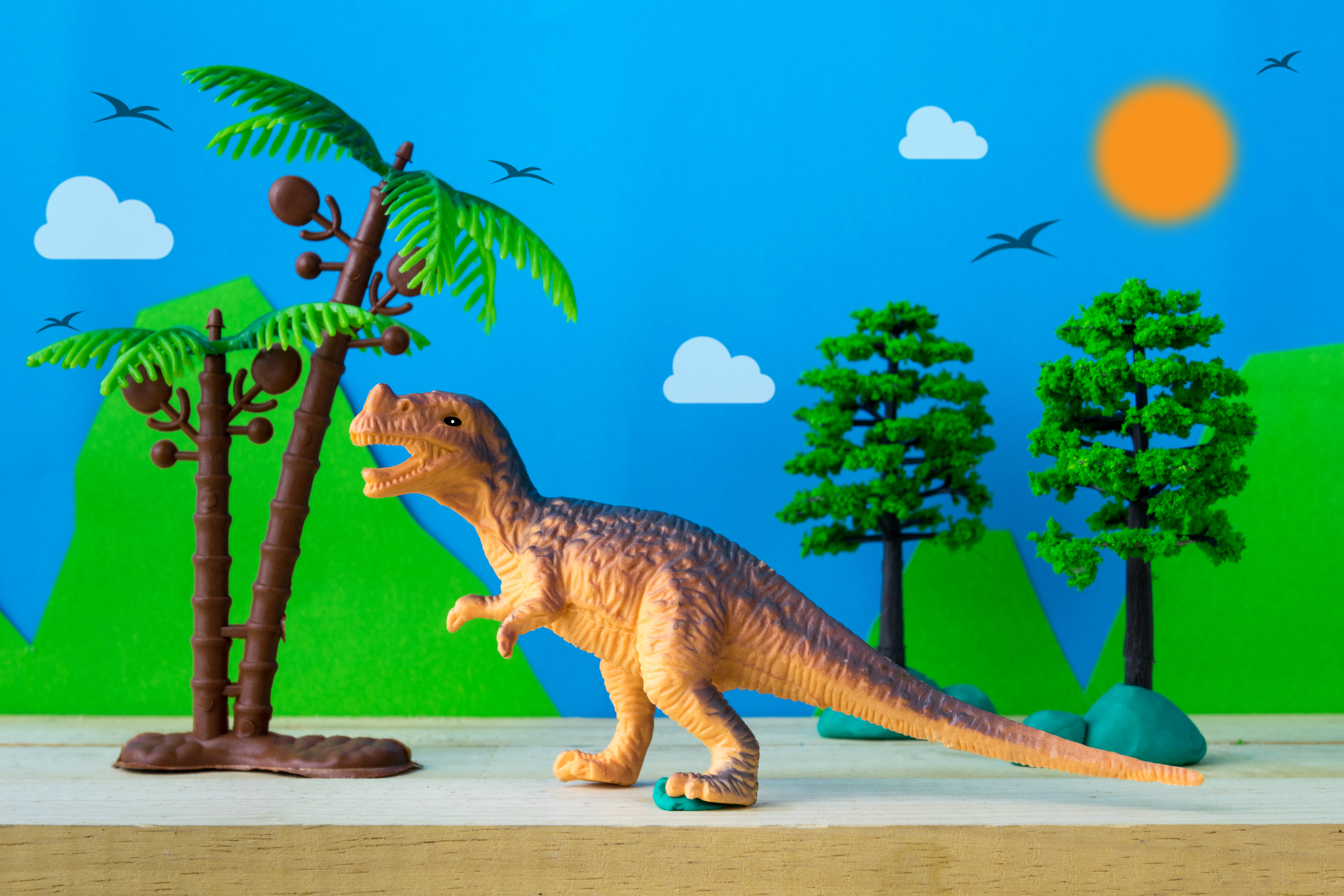 Cover Image: A whimsical diorama featuring a toy T-Rex and toy trees with a paper cutout background featuring mountains, a sky, birds, and a sun. The image references the different ways humans can represent reality.